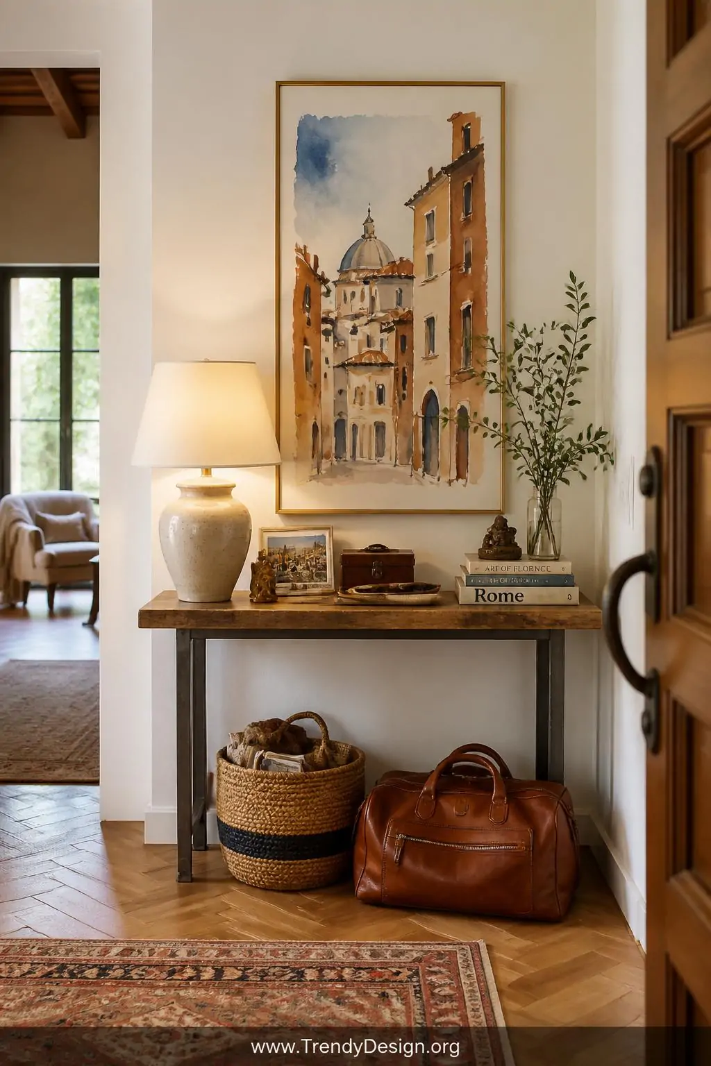 A warmly lit entryway with herringbone hardwood floors and a console table topped with a ceramic lamp and small travel mement