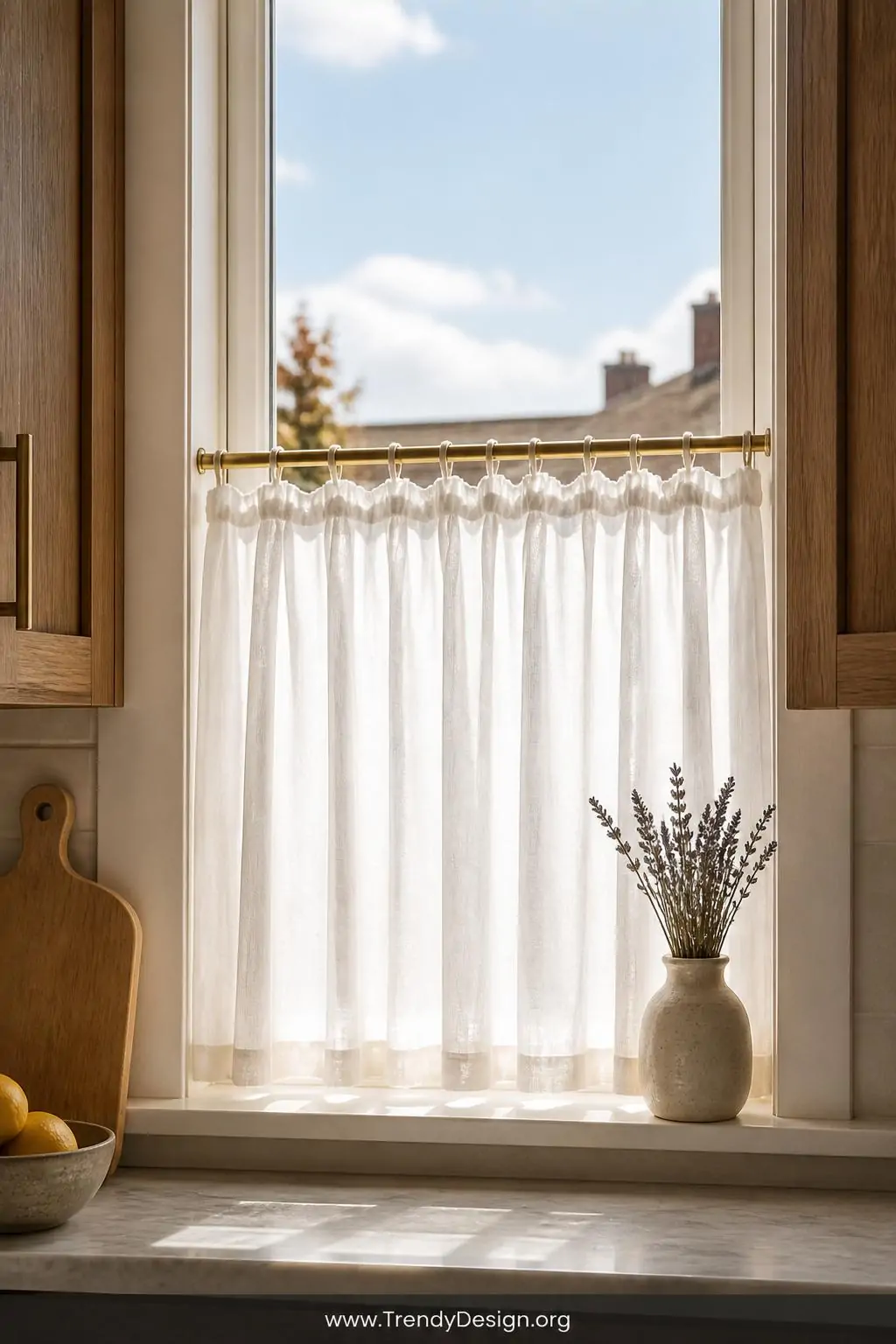 Closeup medium shot of a sun-washed kitchen window fitted with short café-style white sheer panels hanging from a thin matte