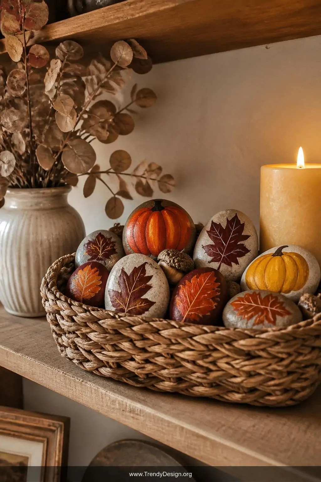 A medium shot of a rustic autumn-styled kitchen shelf displaying a collection of seasonal painted rocks featuring pumpkins, a