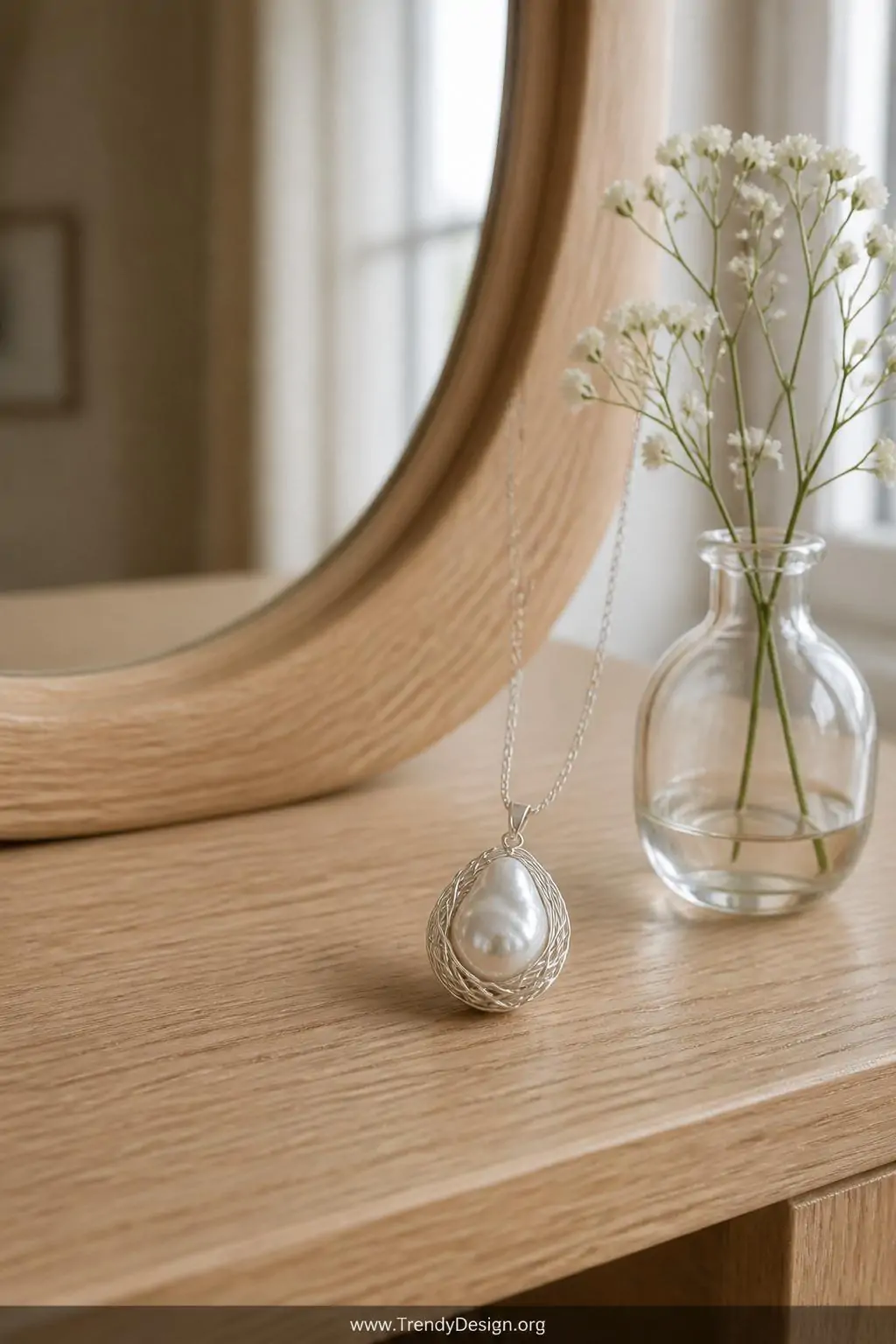 Baroque freshwater pearl pendant cradled in a fine silver wire nest displayed beside a small glass bud vase on a light oak vanity, soft diffused afternoon light, medium shot showcasing the pearl's natural luster against warm wood tones