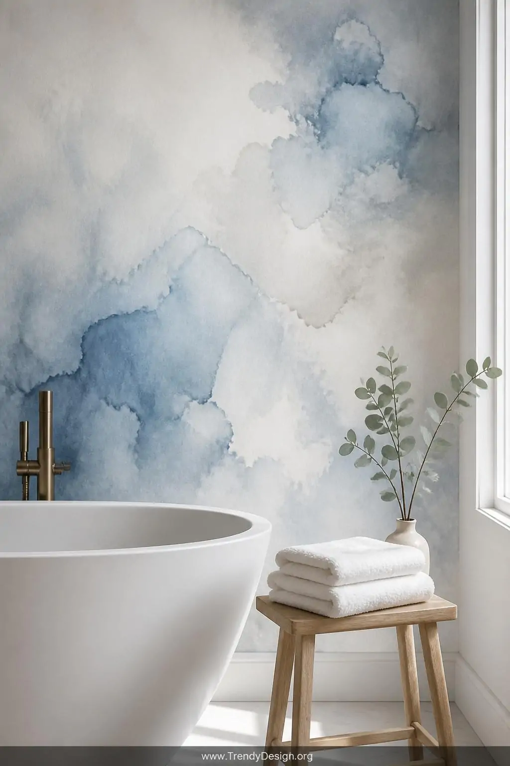 Soft watercolor-wash wallpaper in misty blue, pale white, and watery gray covering a serene bathroom wall behind a simple white soaking tub, crisp white folded towels stacked on a light oak stool, a single eucalyptus sprig in a bud vase catching natural window light, closeup of the luminous painterly texture, photorealistic interior design.
