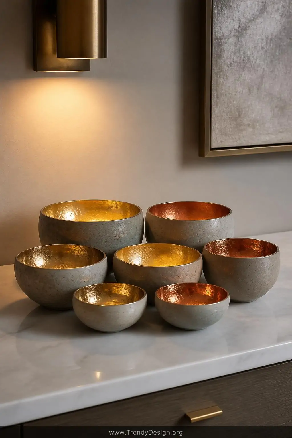 A curated collection of seven tiny concrete bowls in varied sizes with gleaming gold and copper metallic painted interiors is