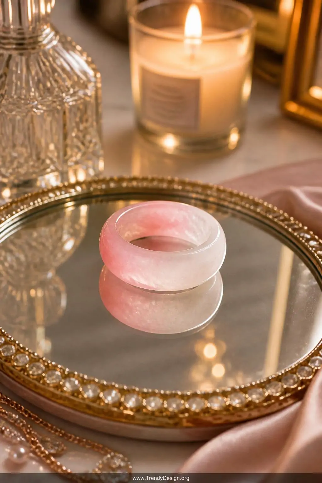 Translucent stone-look polymer clay ring mimicking rose quartz with pink-to-white gradient resting on a mirrored jewelry dish, elegantly styled dressing table with candle glow nearby, luxurious feminine style, closeup shot with backlit warm light passing through the translucent clay