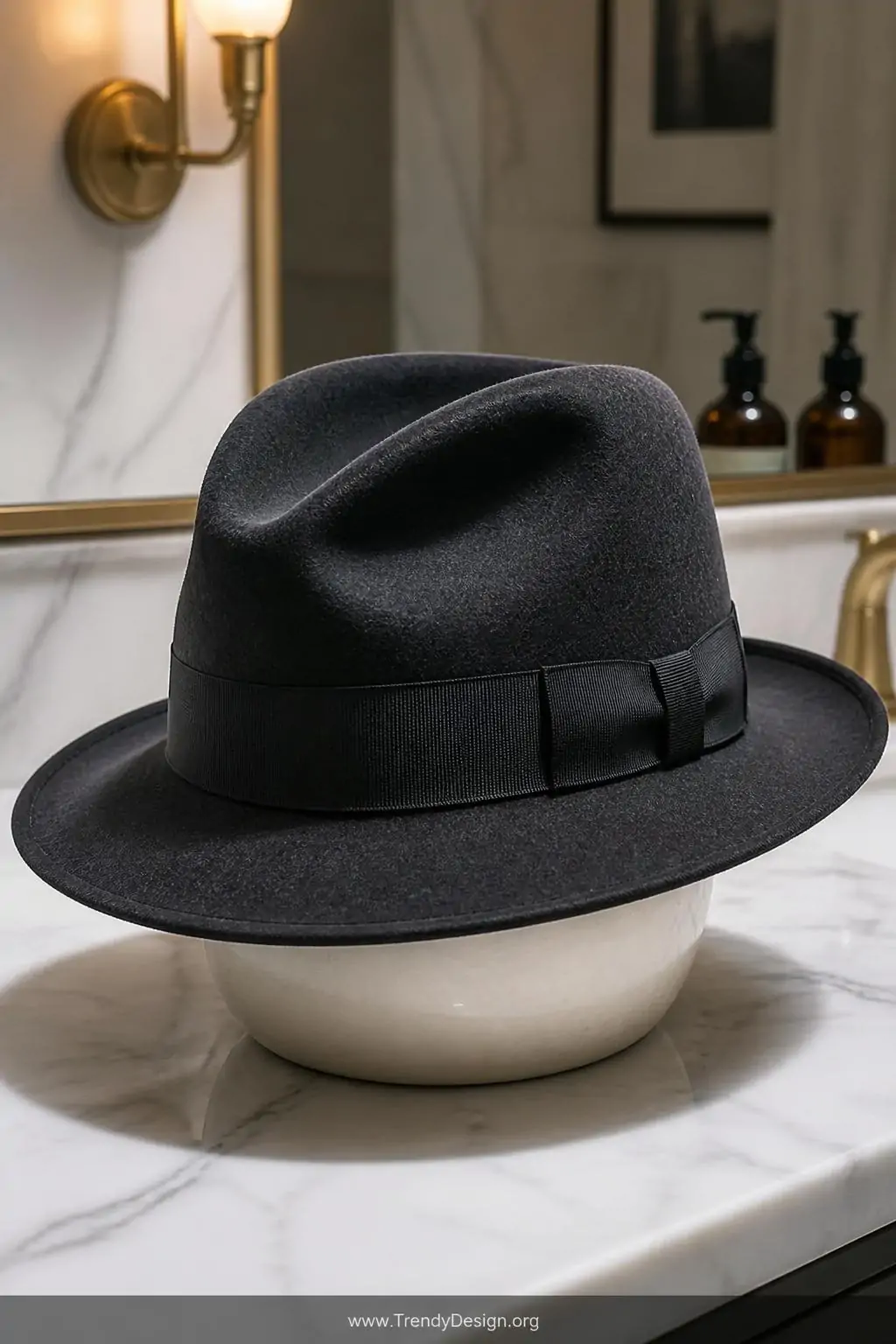 Charcoal wool felt fedora with a black grosgrain ribbon band displayed on a round ceramic bowl hat form on a marble vanity countertop, soft bathroom sconce lighting highlighting the steam-shaped crown and pinched front, closeup shot showing the polished ribbon detail.