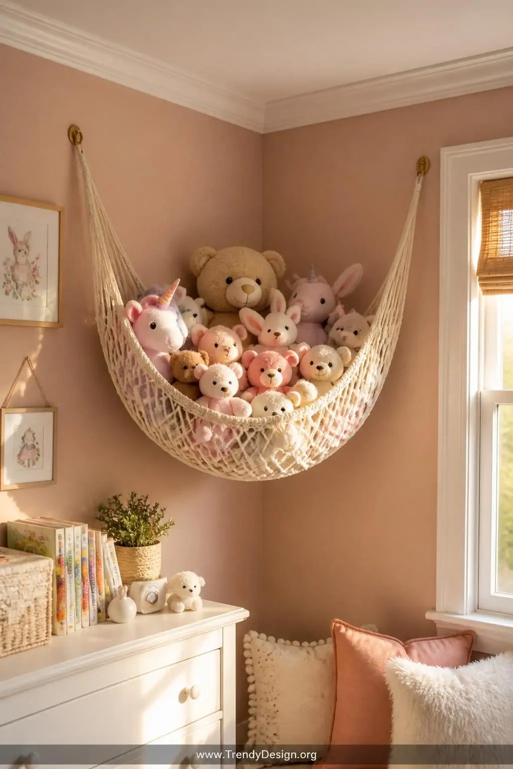 In the upper corner of a whimsical children's bedroom with warm blush pink walls and white trim, a cream-colored macramé toy 