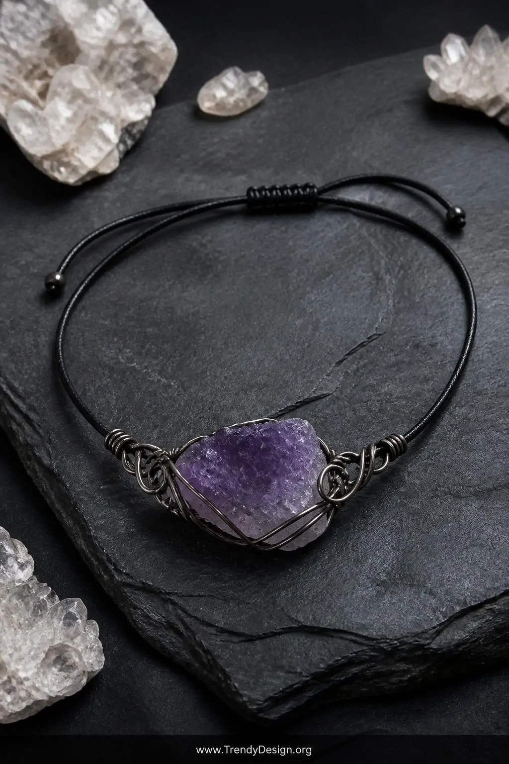 Raw amethyst wire-wrapped crystal choker with sliding knot closure displayed on a dark slate stone surface surrounded by small quartz clusters, cool moody studio lighting, wide shot capturing the organic metallic wrapping and purple crystal focal point